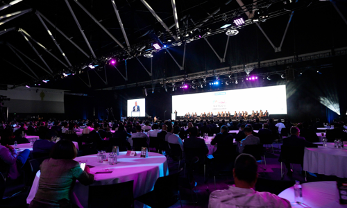 View from back of room full of seated delegates and speaker panel 