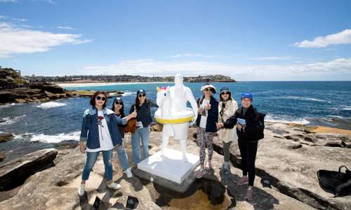 Chinese incentive group take a picture with sculpture at Bondi Beach amidst a backdrop of blue skies and blue seas