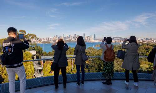 A group of people facing Sydney skyline and taking a photo of the harbour and city