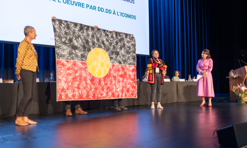 Presenters on stage with indigenous artwork on stage at the ICOMOS event