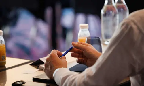 A man at a conference showing his hands on the table holding a pen