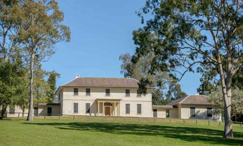 Colonial-style building of Old Government House sits near gum trees on a grassy lawn