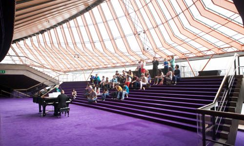 Group of 20 sit on the purple steps at Sydney Opera House during a tour and watch a piano performance