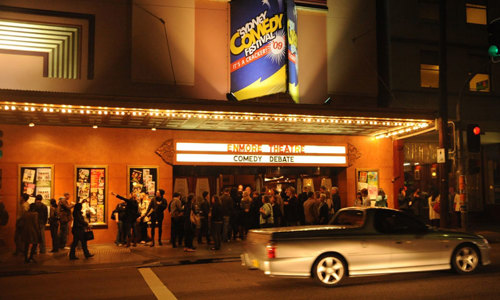 Spectators line up outside Enmore Theatre for a comedy debate. Lights on the building shine in the evening