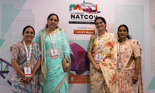 Group of four women delegates in traditional sari outfits, standing in front of the Credai Natcon signage board at entrance